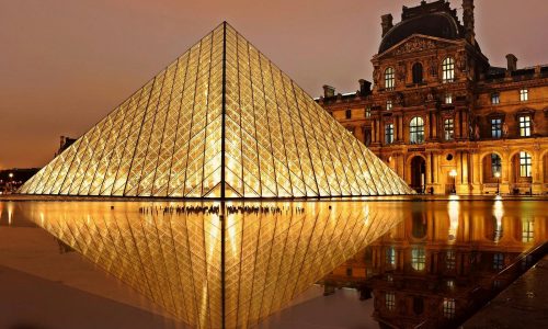 Stunning nighttime view of the illuminated Louvre Pyramid and reflection in Paris, France.