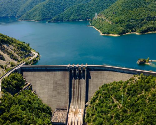 Scenic aerial shot of Vacha Reservoir surrounded by lush green forests and mountains in Bulgaria.