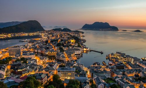Explore the breathtaking skyline of Ålesund, Norway, illuminated against a stunning sunset over the harbor.