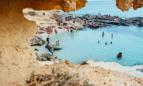 A picturesque beach scene in Spain with people enjoying swimming and sunbathing by rock formations.