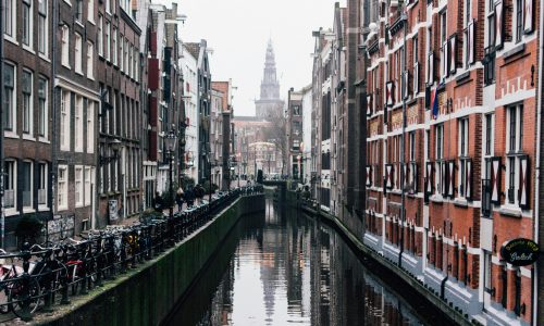 Misty view of a canal with bicycles and historic buildings in Amsterdam.